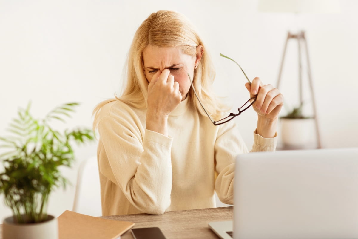 An office worker rubbing her eyes in frustration, illustrating how poor posture and lack of neck support can contribute to eye strain.