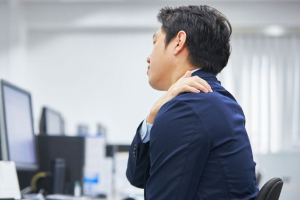 A person experiencing neck and shoulder pain while sitting at a desk.