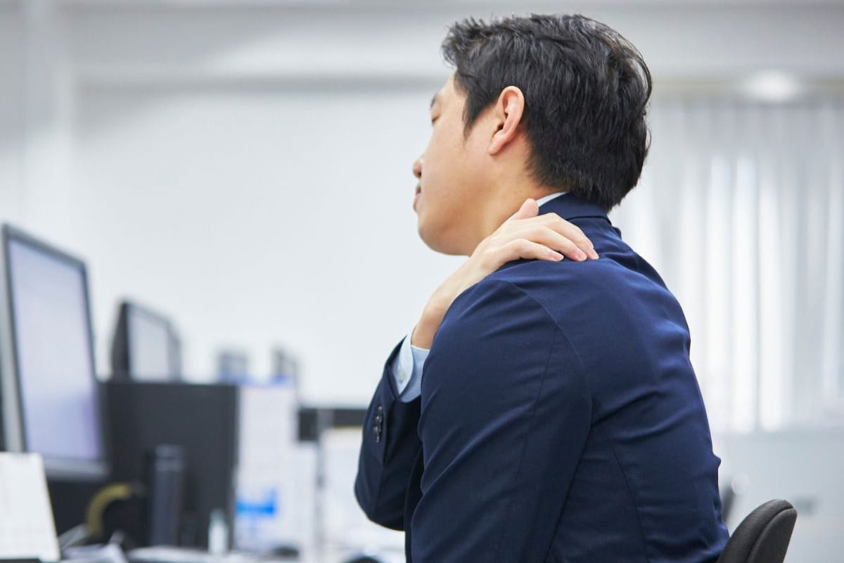 A person experiencing neck and shoulder pain while sitting at a desk.