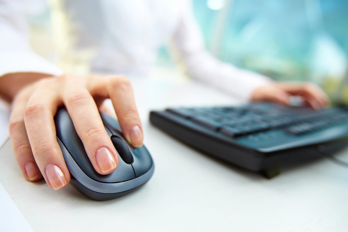 Hand positioned on a mouse beside a keyboard demonstrating proper workstation ergonomics.
