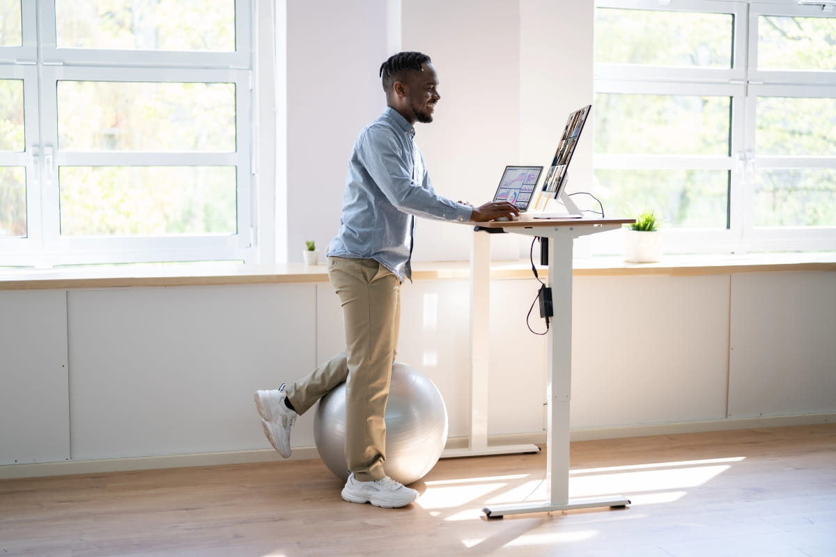 Man using a standing desk with a balance ball to encourage movement and maintain better posture while working.