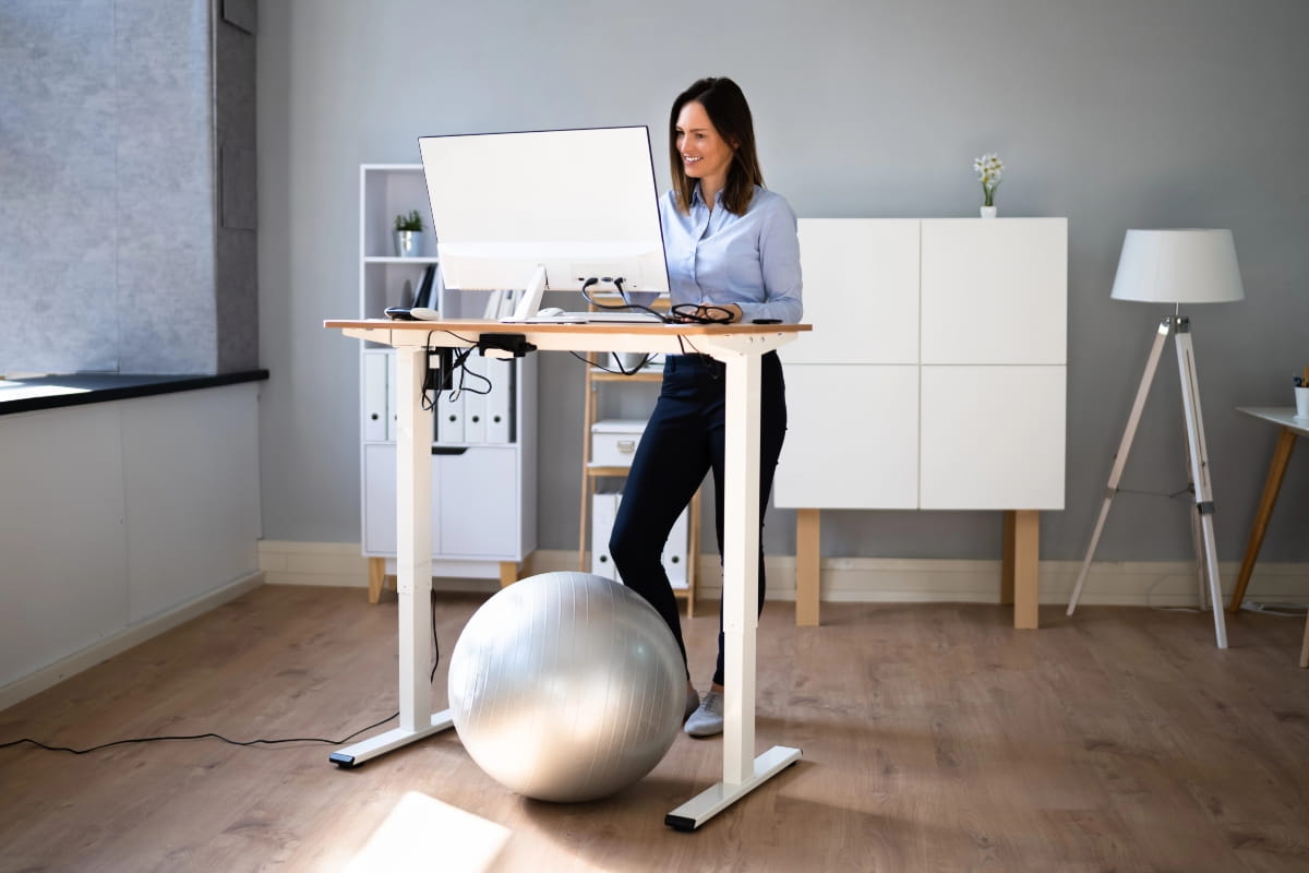 Adjustable desk with monitor, keyboard and exercise ball in a home office.