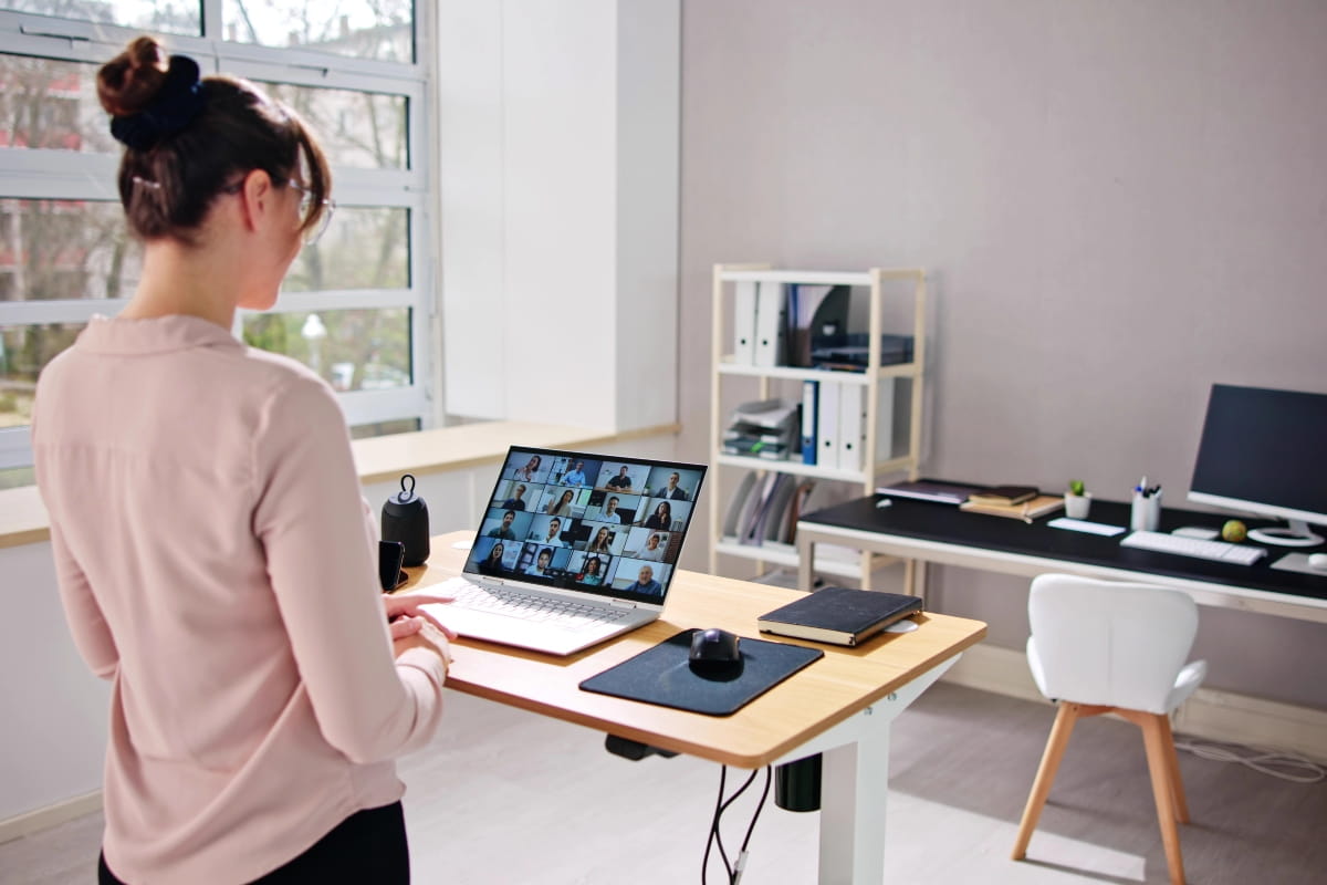Person using a laptop at a standing desk during a video meeting.