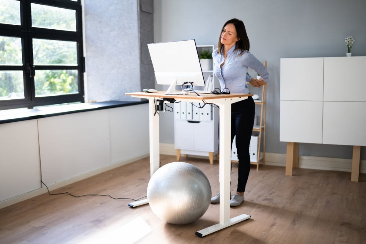 Office worker showing signs of back strain while standing at an adjustable desk.