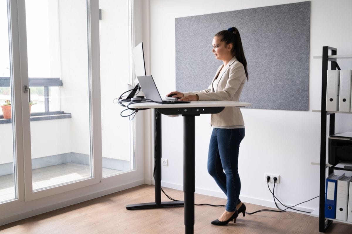 Standing Desk Height: How to Find the Right Setup for You 5 Person standing at an adjustable desk with a laptop, showing a comfortable setup.