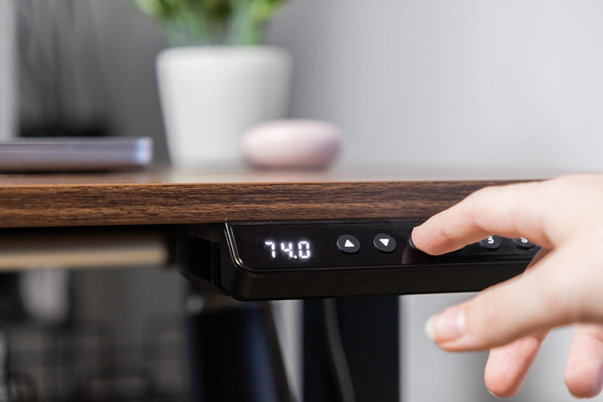 5 Standing Desk Mistakes That Hurt Your Ergonomics 5 Hand adjusting the height controls on an electric standing desk to set a comfortable working position.