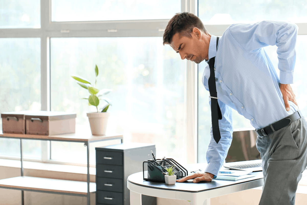 How to Transition to a Standing Desk Without Pain or Fatigue 5 Office worker leaning on a desk with lower back discomfort.
