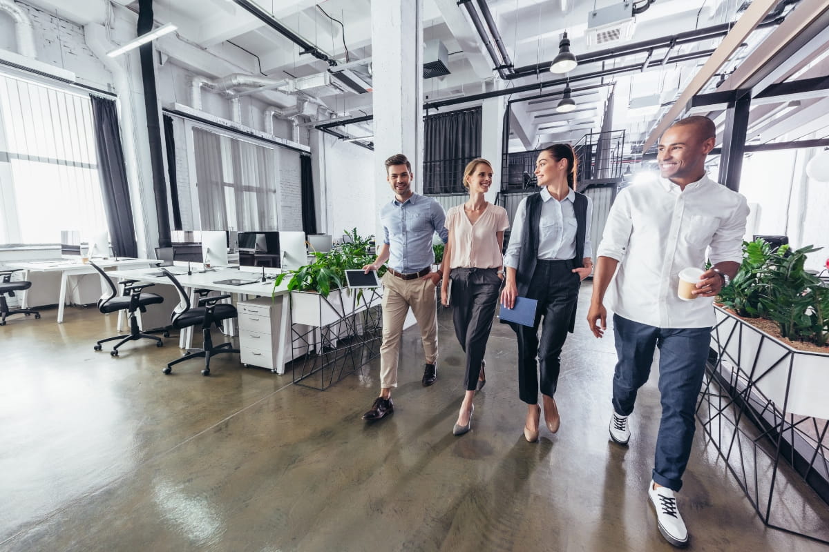 5 Standing Desk Mistakes That Hurt Your Ergonomics 2 Office workers walking through a modern open-plan workplace, taking a movement break away from their desks.