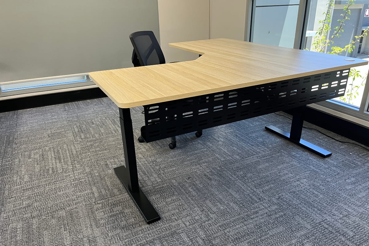 Elevate L-shaped sit-stand desk with a curved inner corner, sturdy black legs and an ergonomic office chair.