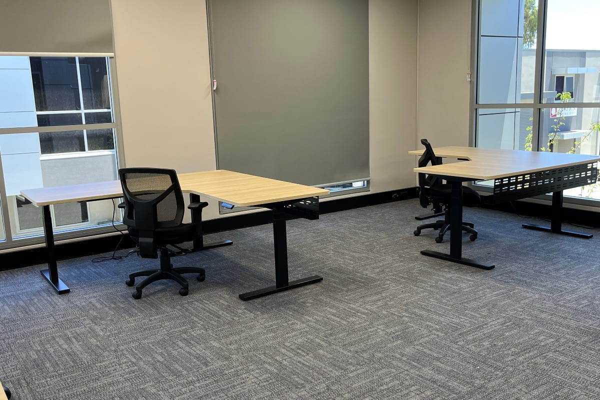 Corner Standing Desk vs Straight Desk: Which Should You Choose? 2 Elevate L-Shape Sit Stand Desks with light wood surfaces and black adjustable frames in a modern office.