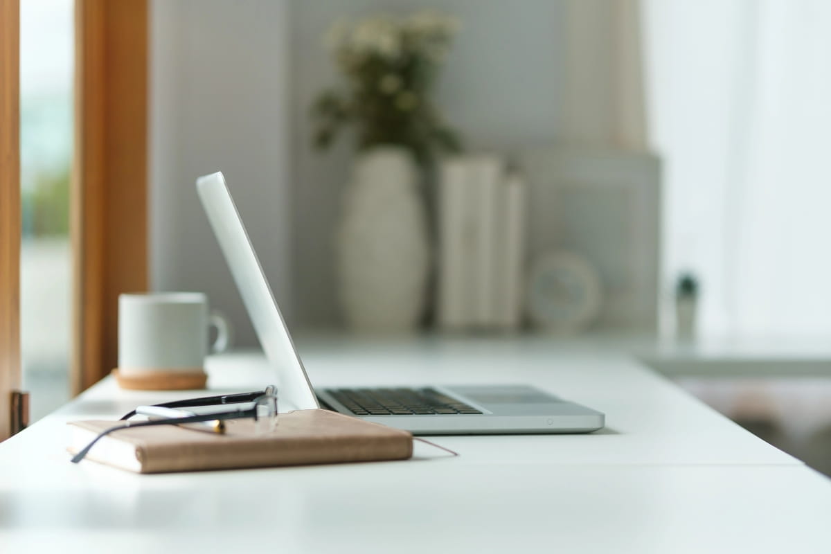 Corner Standing Desk vs Straight Desk: Which Should You Choose? 5 Minimalist L-shape desk setup featuring a laptop, notebook, glasses and coffee mug.
