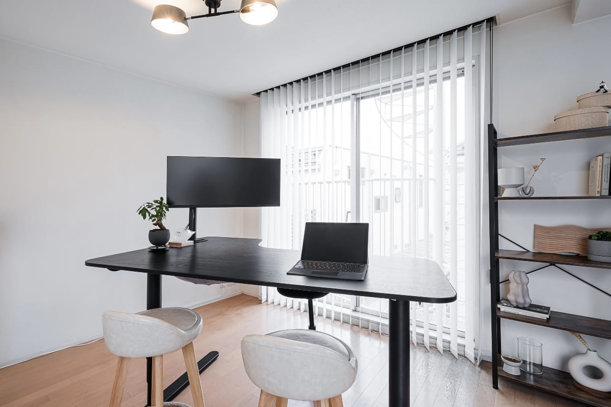 Spacious black height-adjustable desk featuring a curved desktop, computer monitor and laptop in a minimalist workspace.