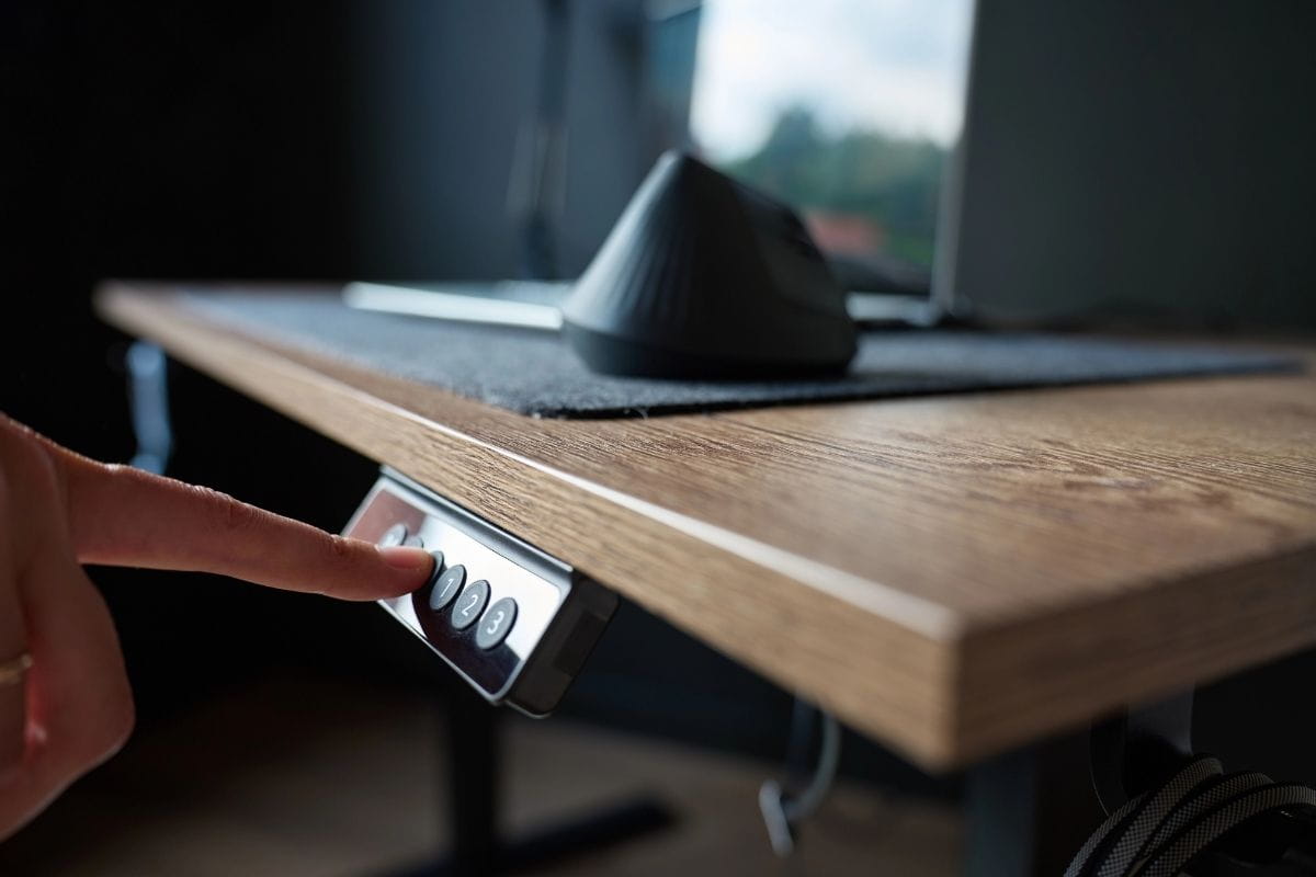 Corner Standing Desk vs Straight Desk: Which Should You Choose? 3 Close-up of a person pressing the height adjustment button on an electric standing desk.