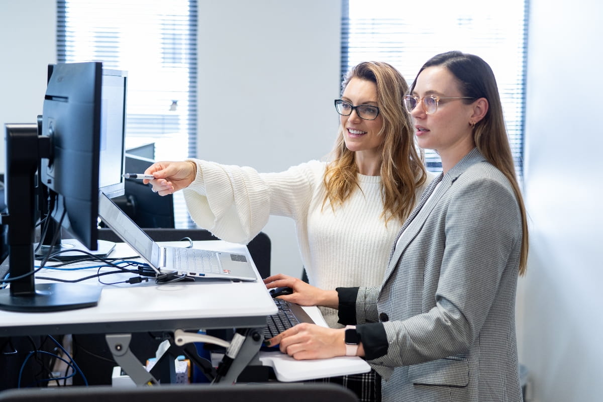 Corner Standing Desk vs Straight Desk: Which Should You Choose? 4 Colleagues working together at a height-adjustable standing desk while reviewing information on a computer screen.