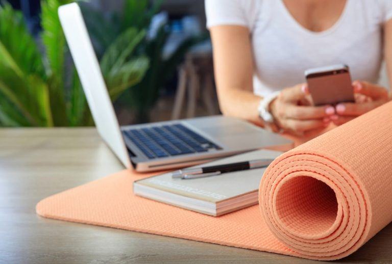 Peach yoga mat for office exercises, with woman working on a laptop in the background.