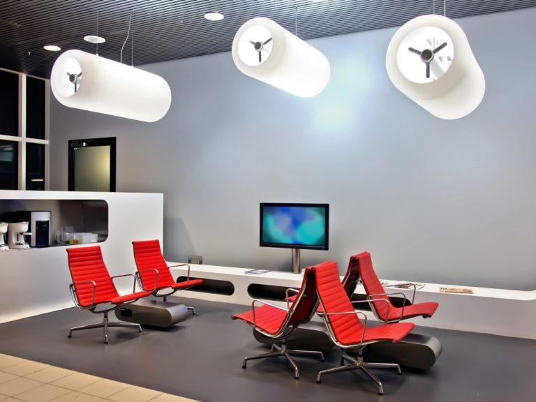 Stylish and functional commercial fitout displaying a clean, modern design with vibrant red lounge chairs, a curved white reception counter, and distinctive white cylindrical ceiling lights.