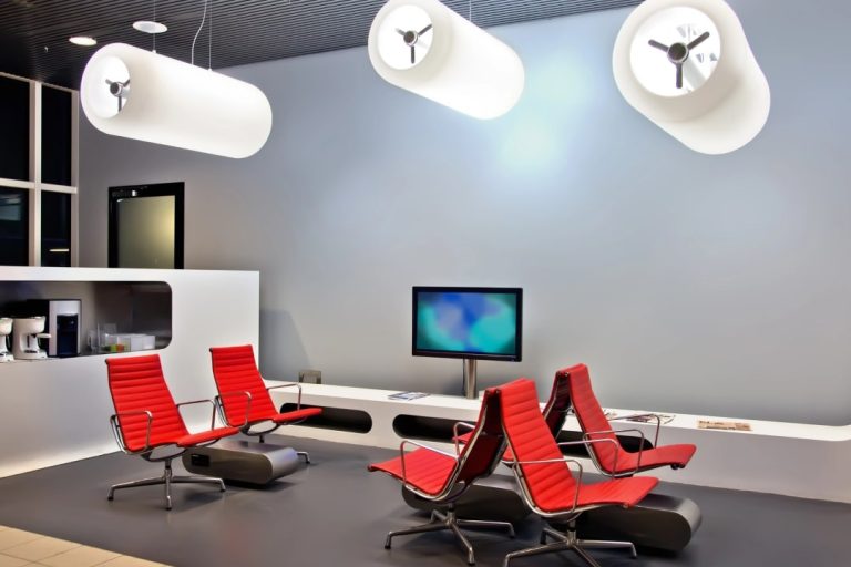 Stylish and functional commercial fitout displaying a clean, modern design with vibrant red lounge chairs, a curved white reception counter, and distinctive white cylindrical ceiling lights.