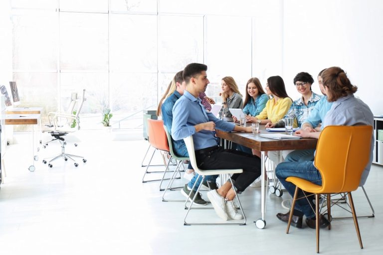 Office team collaborating in a well-lit workspace, featuring a combination of fabric and leather chairs to highlight the contrast in office furniture styles.