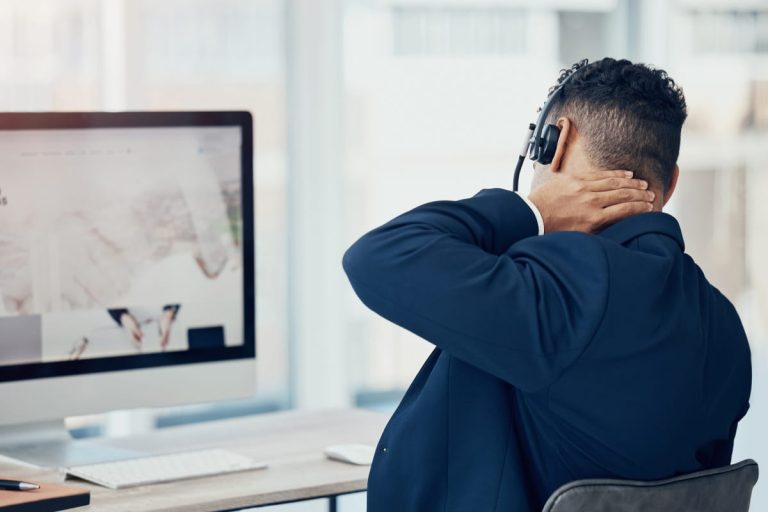 A person experiencing neck pain while sitting at a desk, demonstrating the importance of office chair neck support for reducing discomfort.