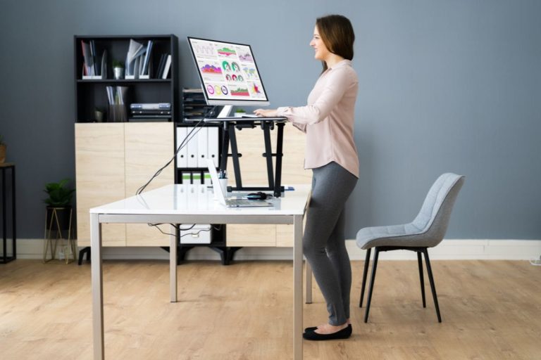Woman using a sit-stand workstation in an office, showing how standing desk mistakes can reduce ergonomic support.