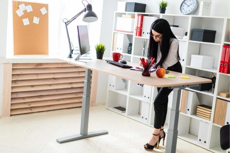 Woman working at a corner standing desk with an adjustable height frame in a bright, organised home office.