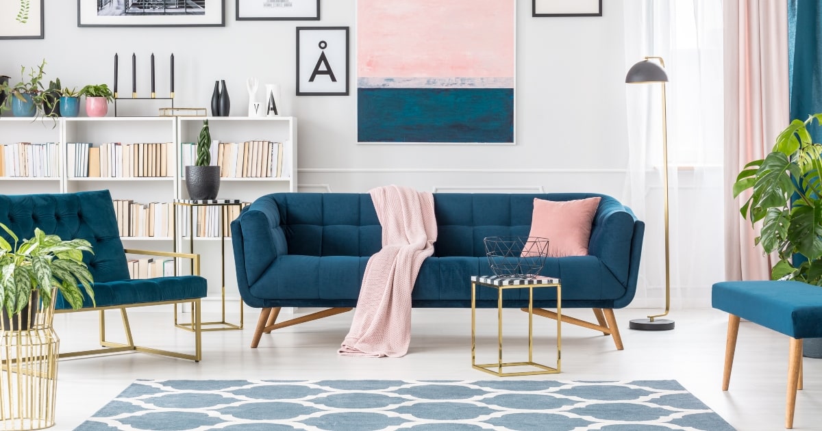 A jewel tone blue couch with pink blanket in elegant living room interior.