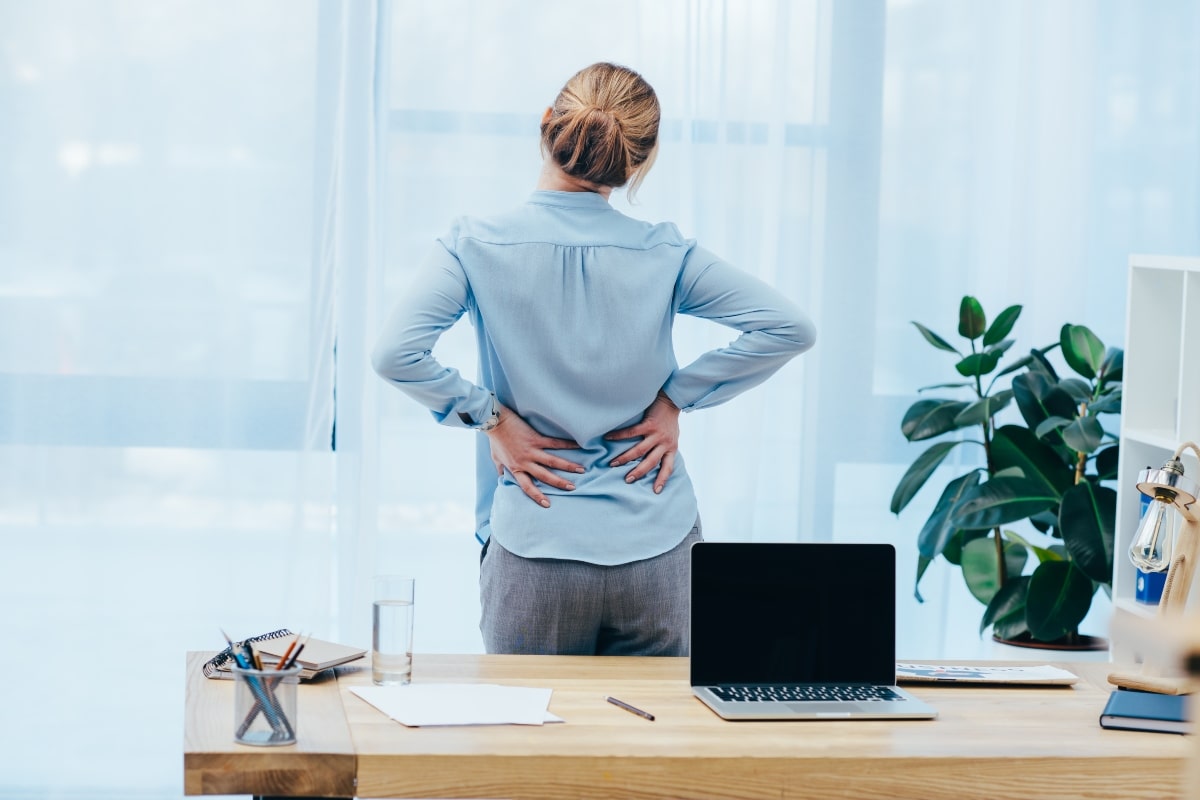 Woman standing at desk with lower back pain.