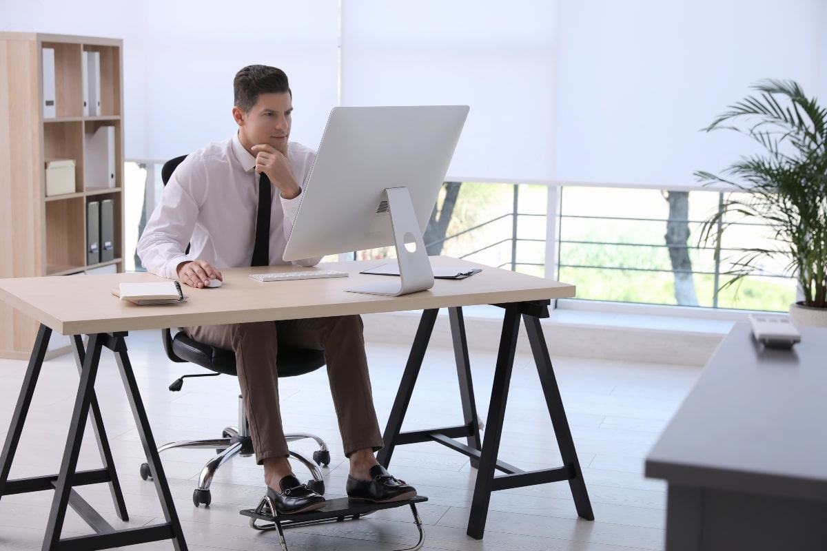Businessman using an adjustable footrest at a desk.