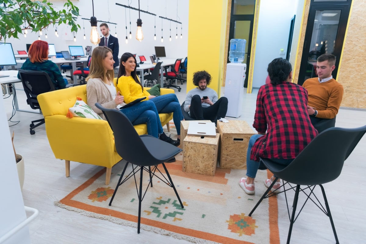Office decorating ideas: A relaxed office with team members sitting in casual space with on bright yellow sofa and accent wall.