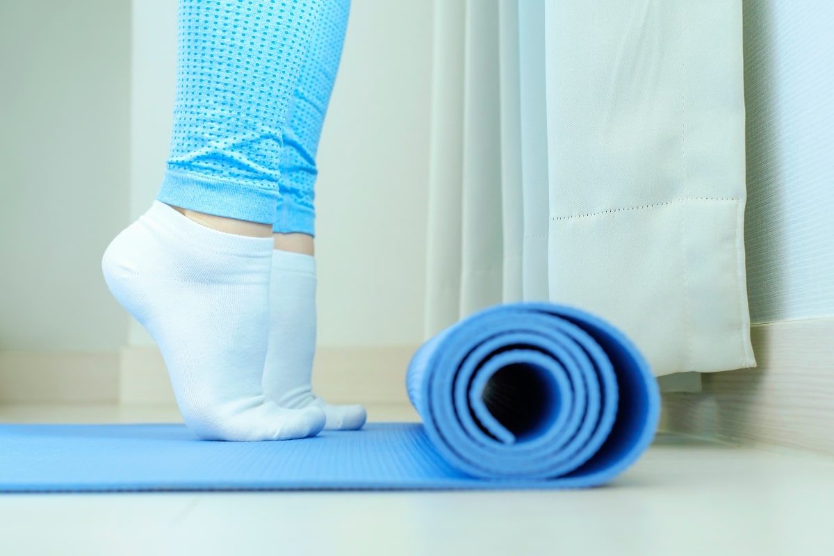 A woman performing calf raises on a yoga mat in her office with socks on, highlighting the benefits of office exercises. 