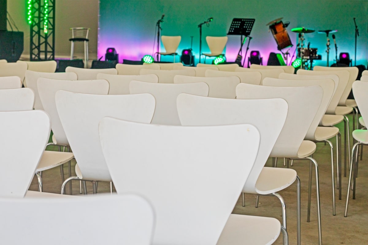 An image illustrating a seating plan, with rows of white chairs neatly aligned, all facing a central stage or focal point, representing a formal and organised event setup.