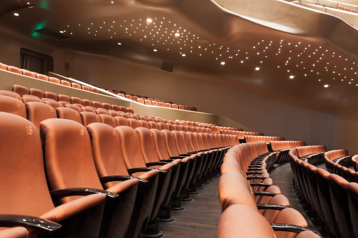 An illustrative image demonstrating a theatre seating arrangement, with rows of chairs facing towards a stage, resembling a classic theatre or auditorium setup.